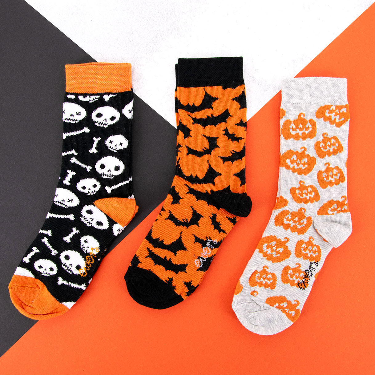 Halloween Herbst Socken mit Motiv Totenkopf/Schädel, Kürbis, Fledermäuse Halloween Herbst in orange, schwarz und weiß vor orangem, schwarzen und weißen Hintergrund.