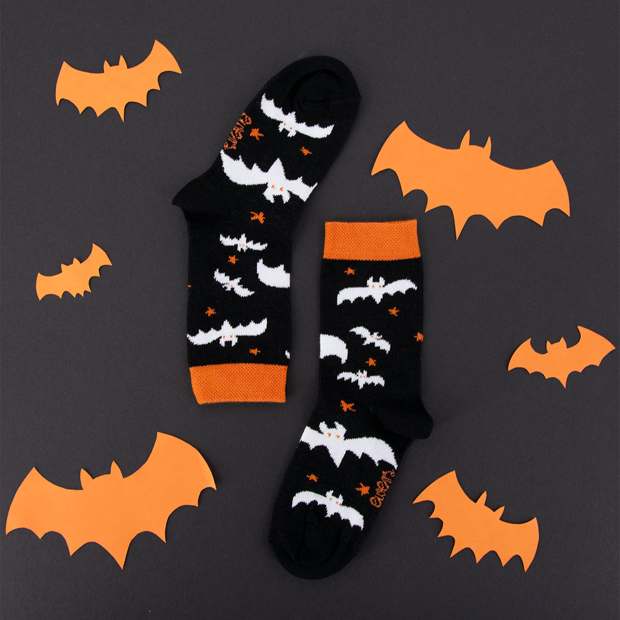 Halloween Herbst Socken schwarz mit weißem Motiv Fledermaus und Sterne orange auf Hintergrund in dunkelgrau mit orangen Fledermäusen.