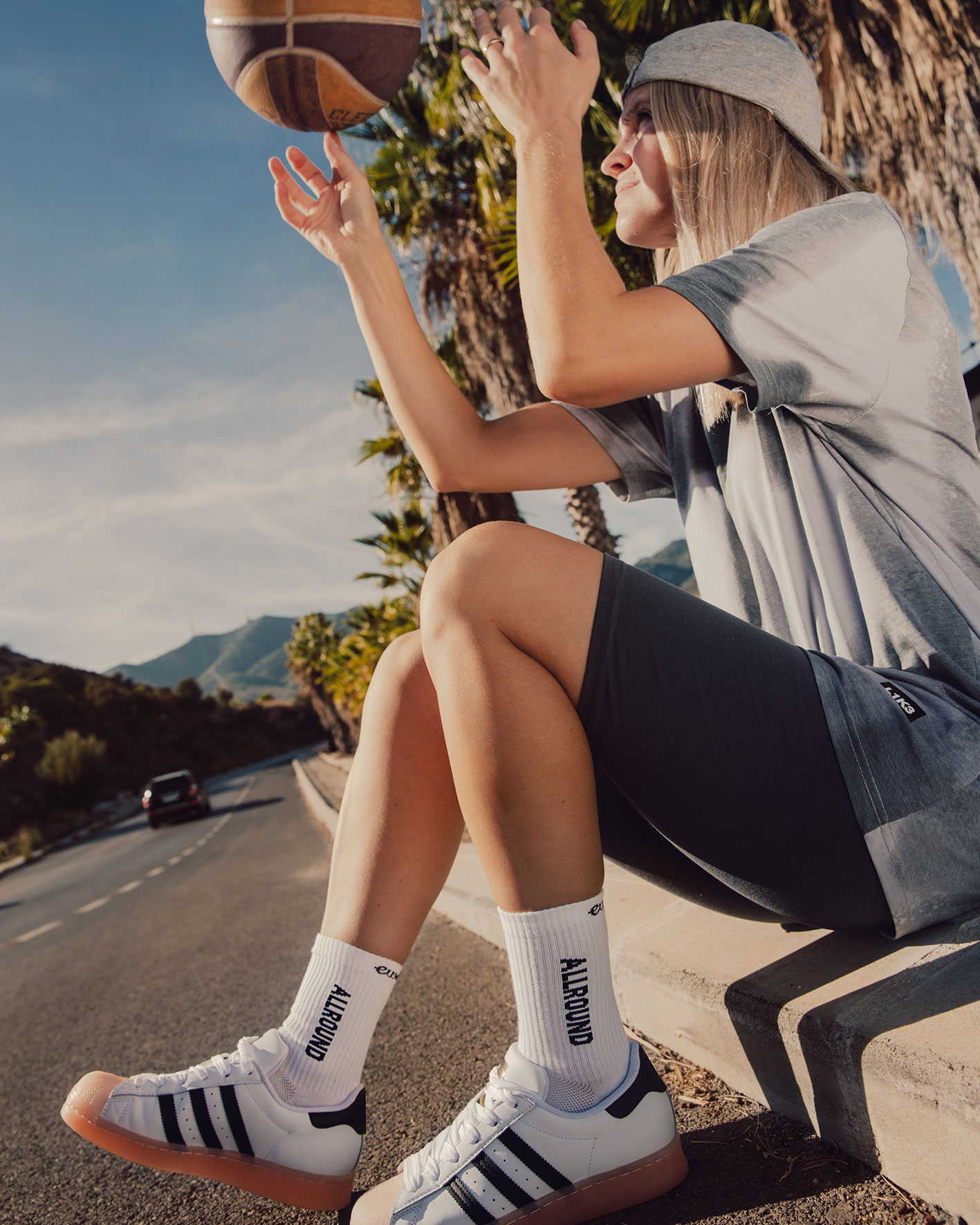 Frau mit Basketball am Straßenrand sitzend, sportlich gekleidet mit Tennissocken Allround, Farbe weiß. Elastisch. Gepolsterte Sohle. Ergonomische Anpassung. Schnell trocknend.