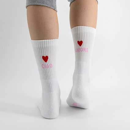 Füße mit Socken in weiß und von hinten mit 2 roten Herzen, Aufschrift rosa "Ciao Amore". Ciao links, Amore rechts.