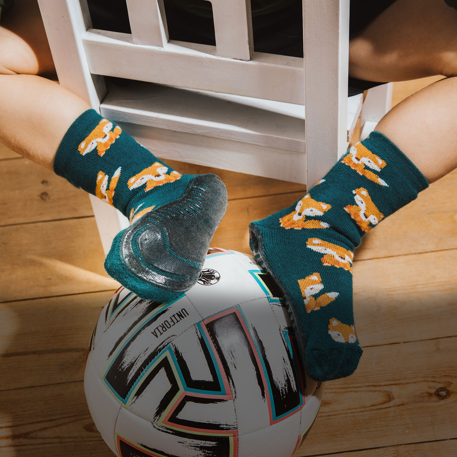 Junge auf Stul sitzend mit Fussball und Stoppersocken SoftStep grün mit Fuchsmotiv