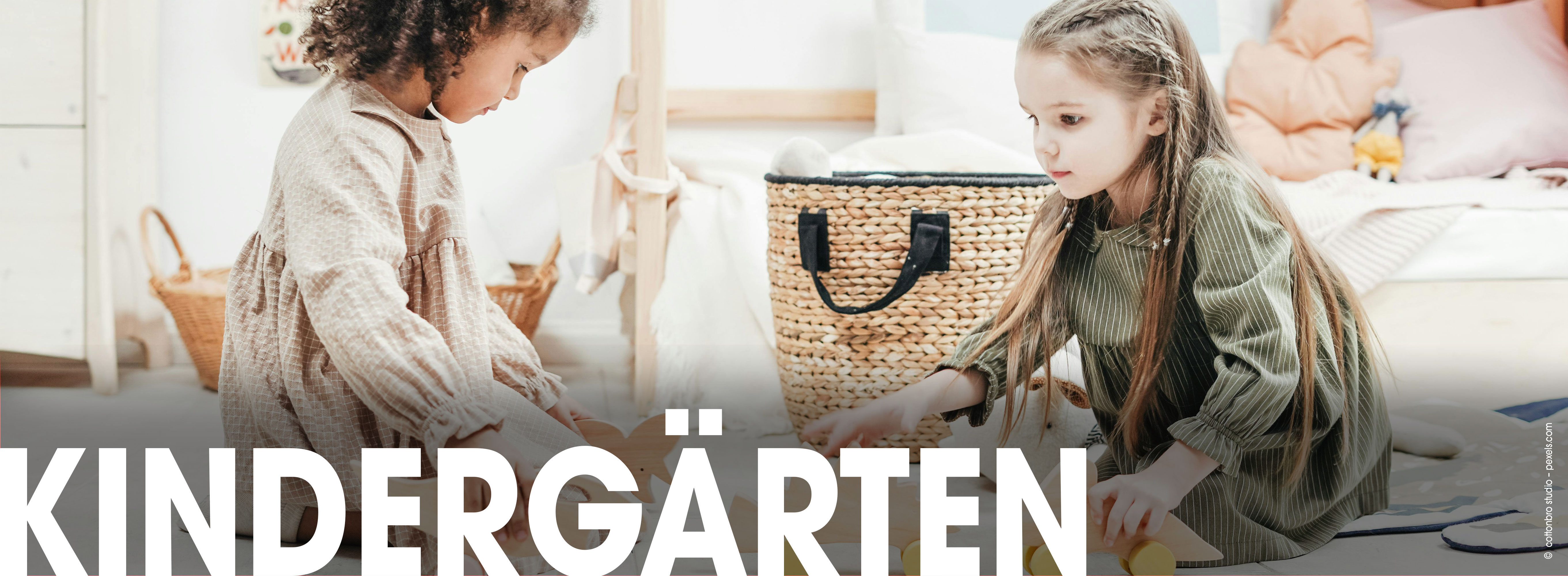 Zwei Kinder im Kindergarten/ in der KITA vor mehreren Körben und Spielzeug in Blusen. Aufschrift Kindergärten.