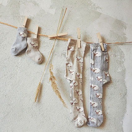 Wäscheleine mit Leinentuch im Hintergrund zwei Strumpfhosen und zwei Socken in Farben Beige/Grau mit Eulen Motiv mit Wäschklammern befestigt.