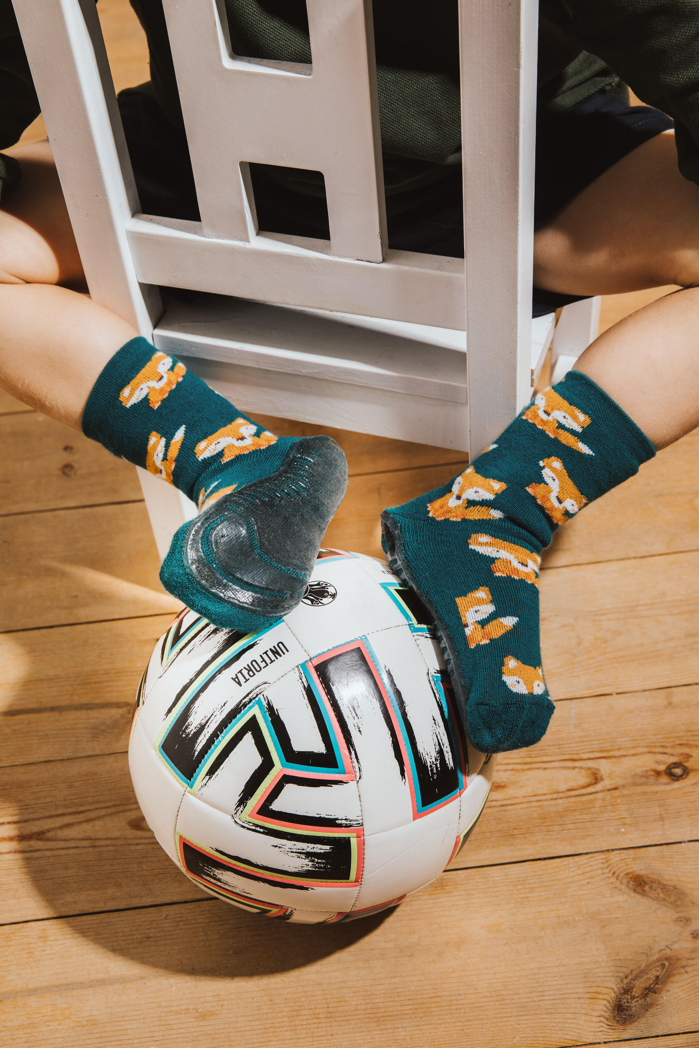 Junge auf Stuhl sitzend mit Fußball und Stoppersocken SoftStep Grün mit Fuchsmotiv