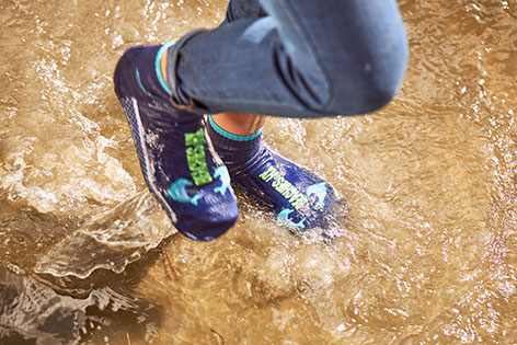 Kinderfüße im Meer planschend in Jeans mit den Beachies in Blau und mit Delfinen.