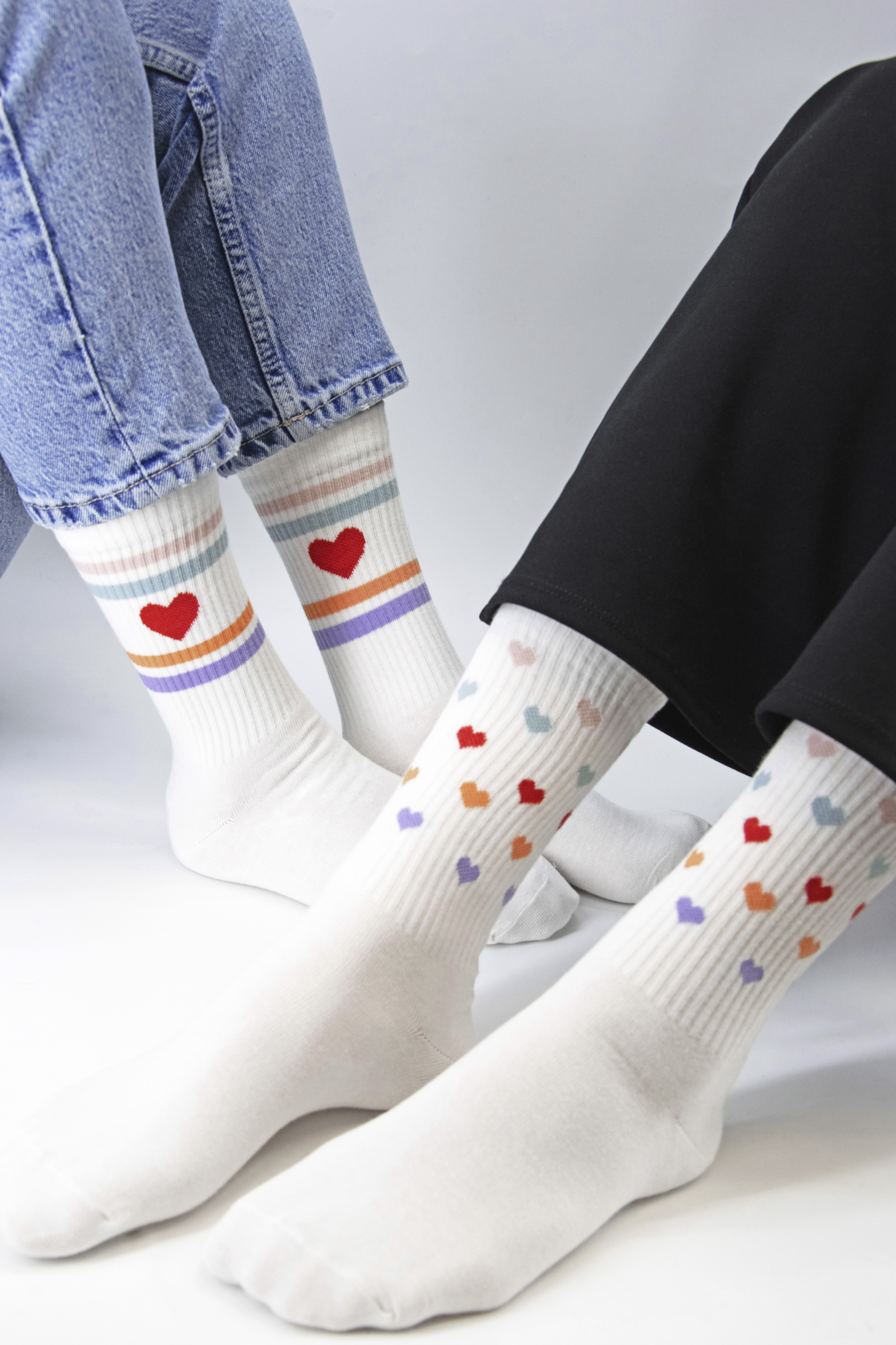 Eine Frau im Vordergrund trägt ein Paar Tennissocken mit kleinen Herzen, eine Frau im Hintergrund trägt ein Paar mit Ringeln und einem Herz.